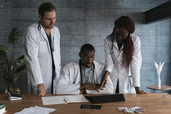 Three people in medical scrubs review reading material at a desk.