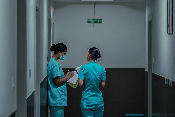two women in scrubs consult with each other in an institutional hallway